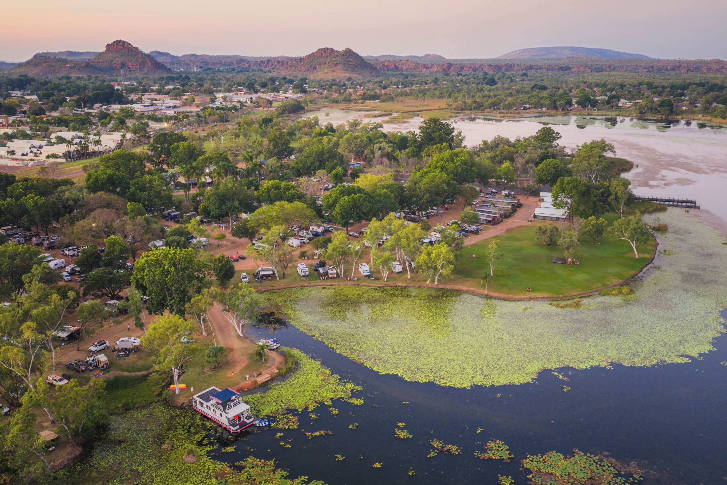 An aerial view of a campsite with RVs, a boat docked by the water, and surrounding greenery.