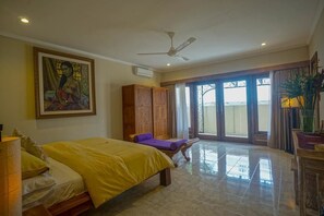Une chambre à coucher avec un lit, un ventilateur de plafond, une grande fenêtre et un tableau accroché au mur.