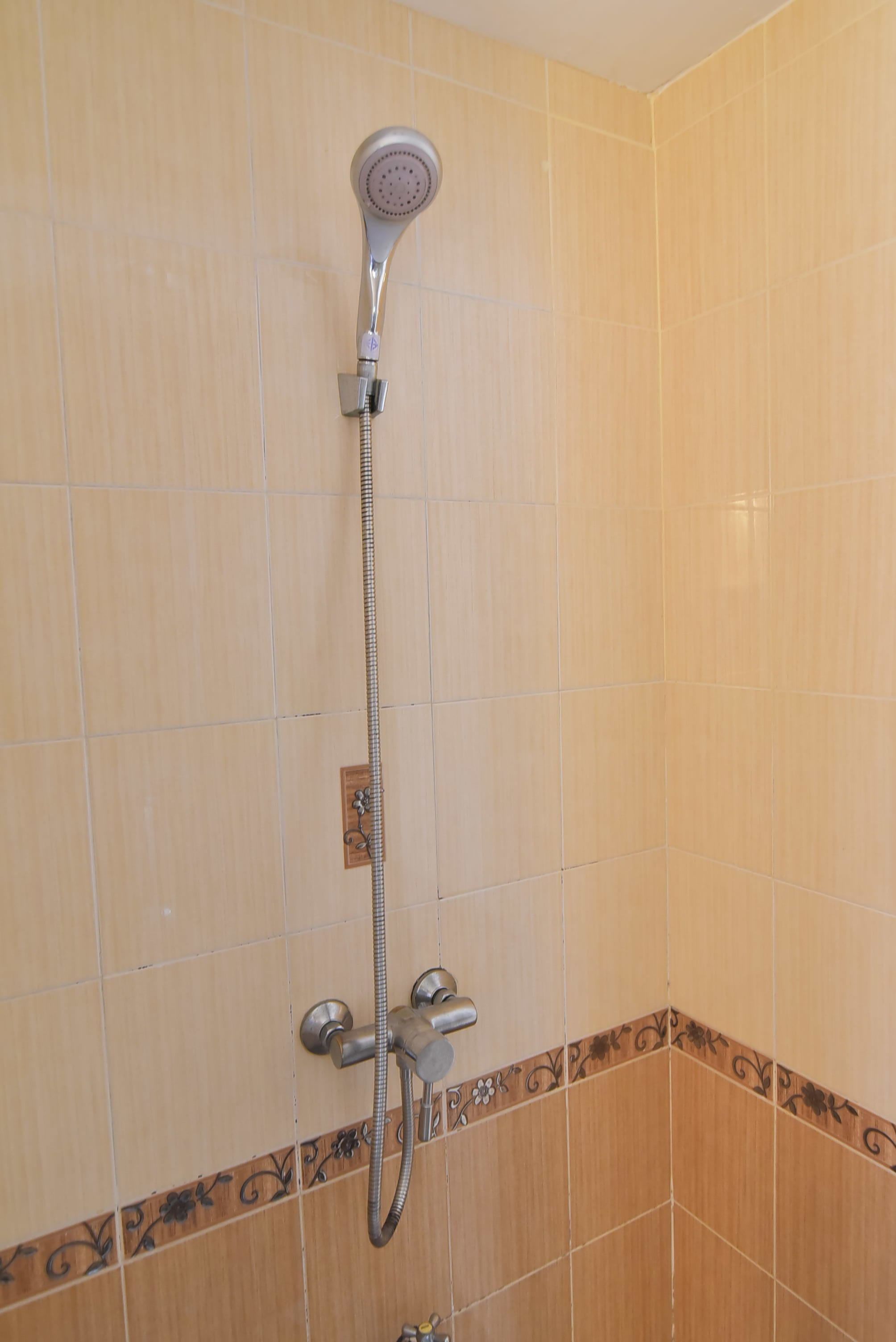 A bathroom with beige tiles, a showerhead, and a handheld shower attachment.