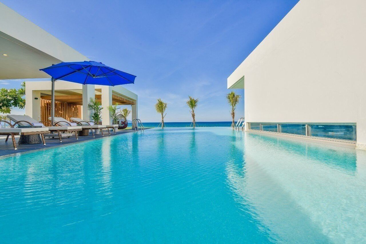 A swimming pool with lounge chairs and umbrellas, surrounded by palm trees and a clear sky.