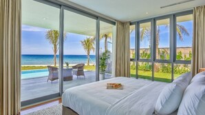 Une chambre avec un grand lit, une vue sur la plage et un balcon aménagé avec du mobilier d’extérieur.