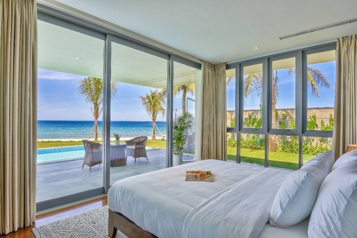 Een slaapkamer met een groot bed, uitzicht op het strand en een balkon met tuinmeubilair.