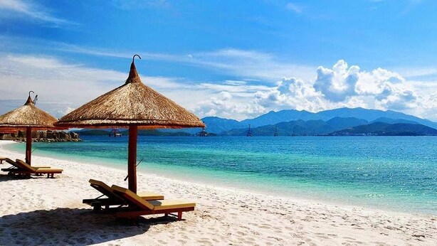 Une plage avec des parasols en chaume et des chaises longues en bois.