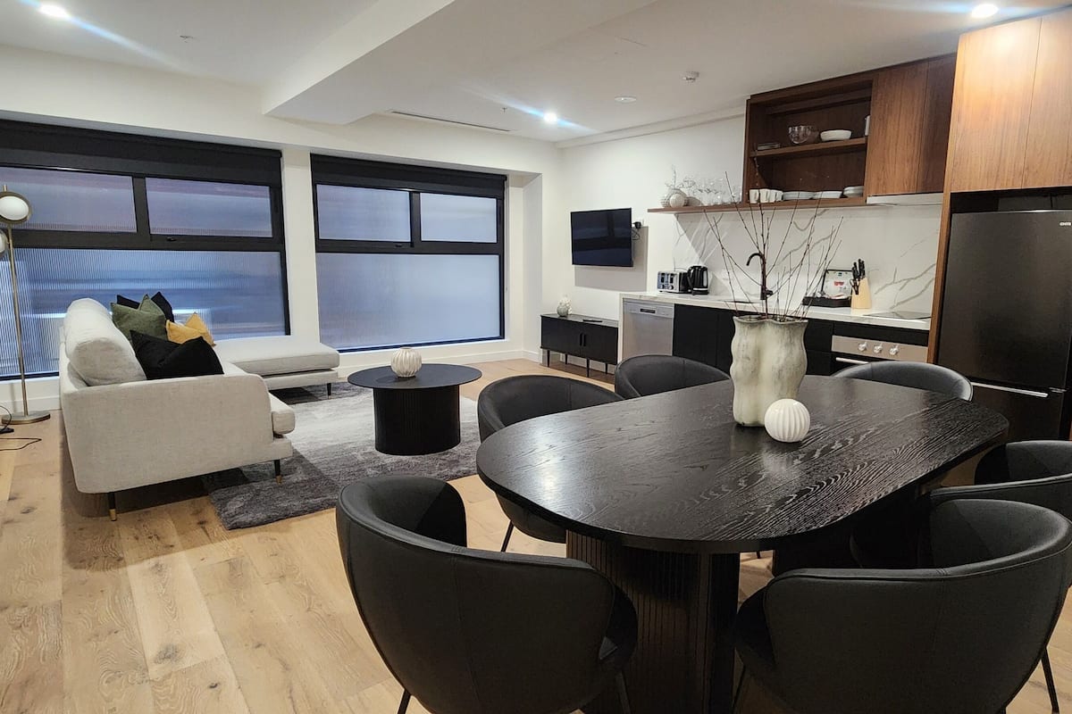 Una sala de estar moderna con un sofá, una mesa de comedor con sillas y una zona de cocina con televisión y armarios.