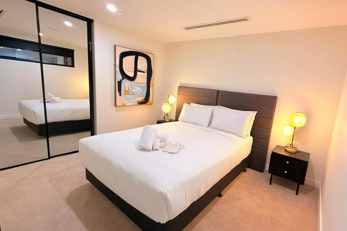 Una habitación de hotel moderna con una cama grande, lámparas de noche, un espejo y una obra de arte en la pared.