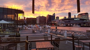 A waterfront restaurant with outdoor seating, overlooking a river and city skyline at sunset. - Absolute Collins Apartments (Melbourne)