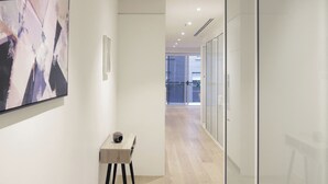 A modern hallway with a minimalist design, featuring a wooden table with a cup, a large abstract painting, and glass doors leading to a balcony. - Absolute Collins Apartments (Melbourne)