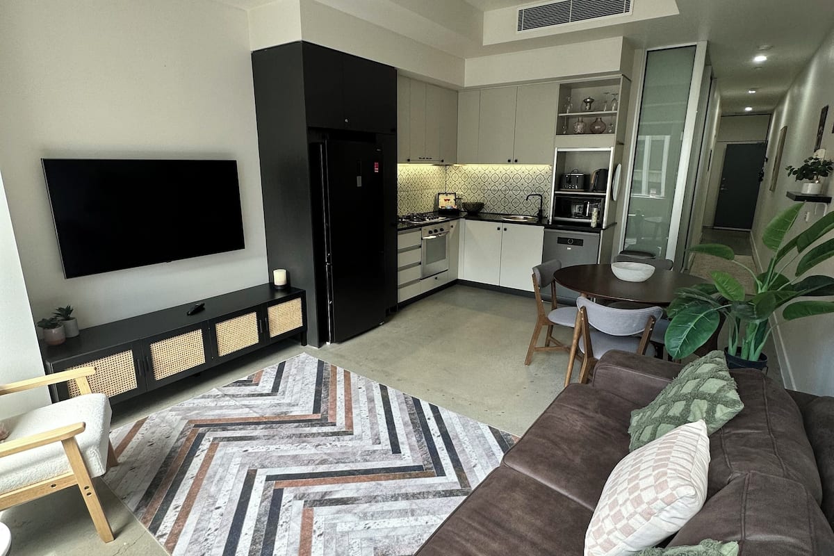 Una sala moderna con un sofá, televisión y una cocina al fondo.