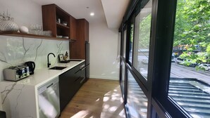 A modern kitchen with a built-in dishwasher, wooden cabinets, and a large window offering a view of the street. - Absolute Collins Apartments (Melbourne)