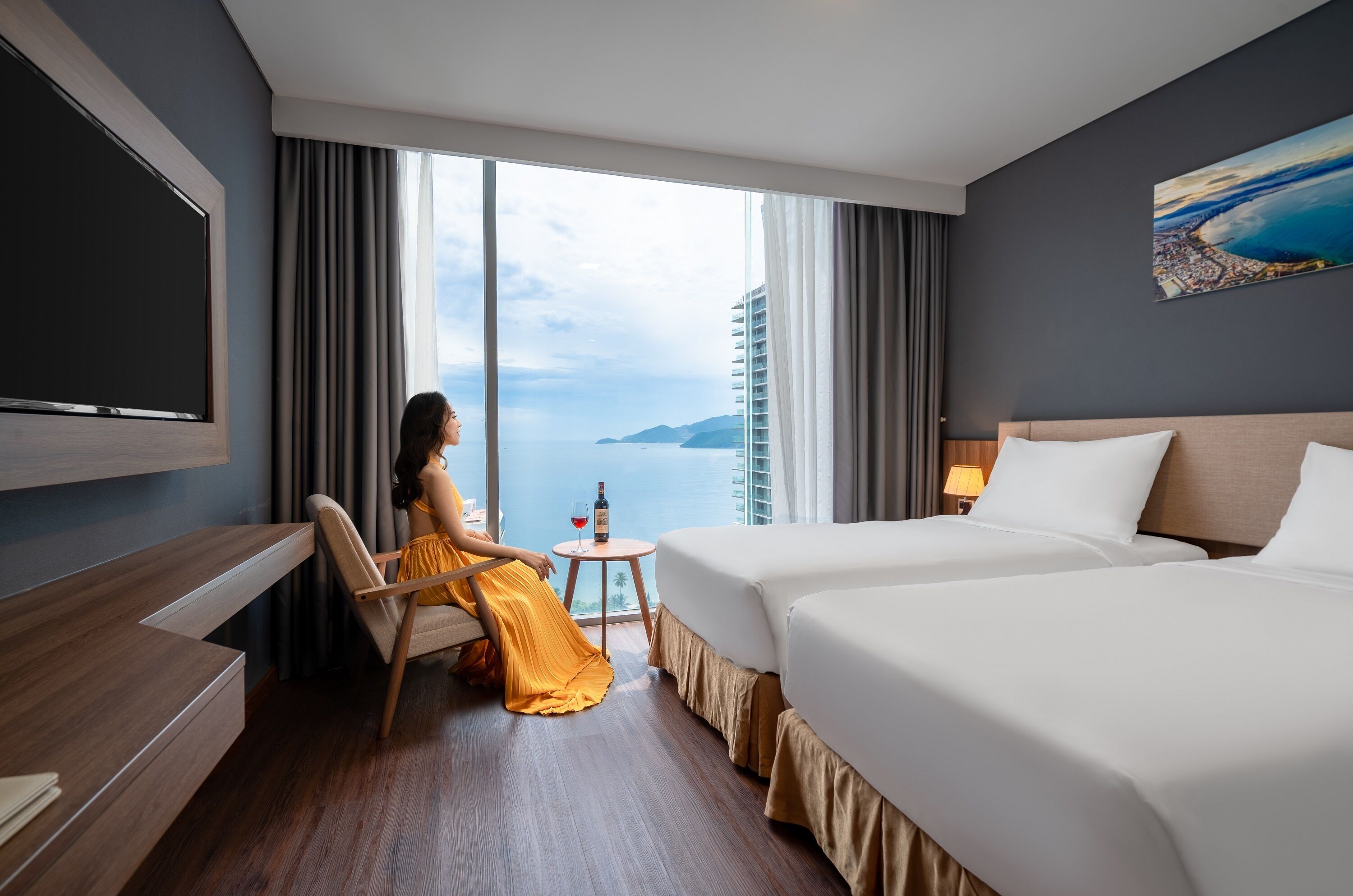 A hotel room with a large window, a bed, a desk, and a chair.