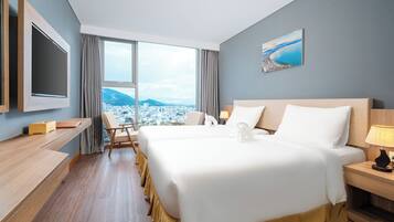 A hotel room with a large bed, a desk, a chair, a TV, and a window with a city and mountains view.