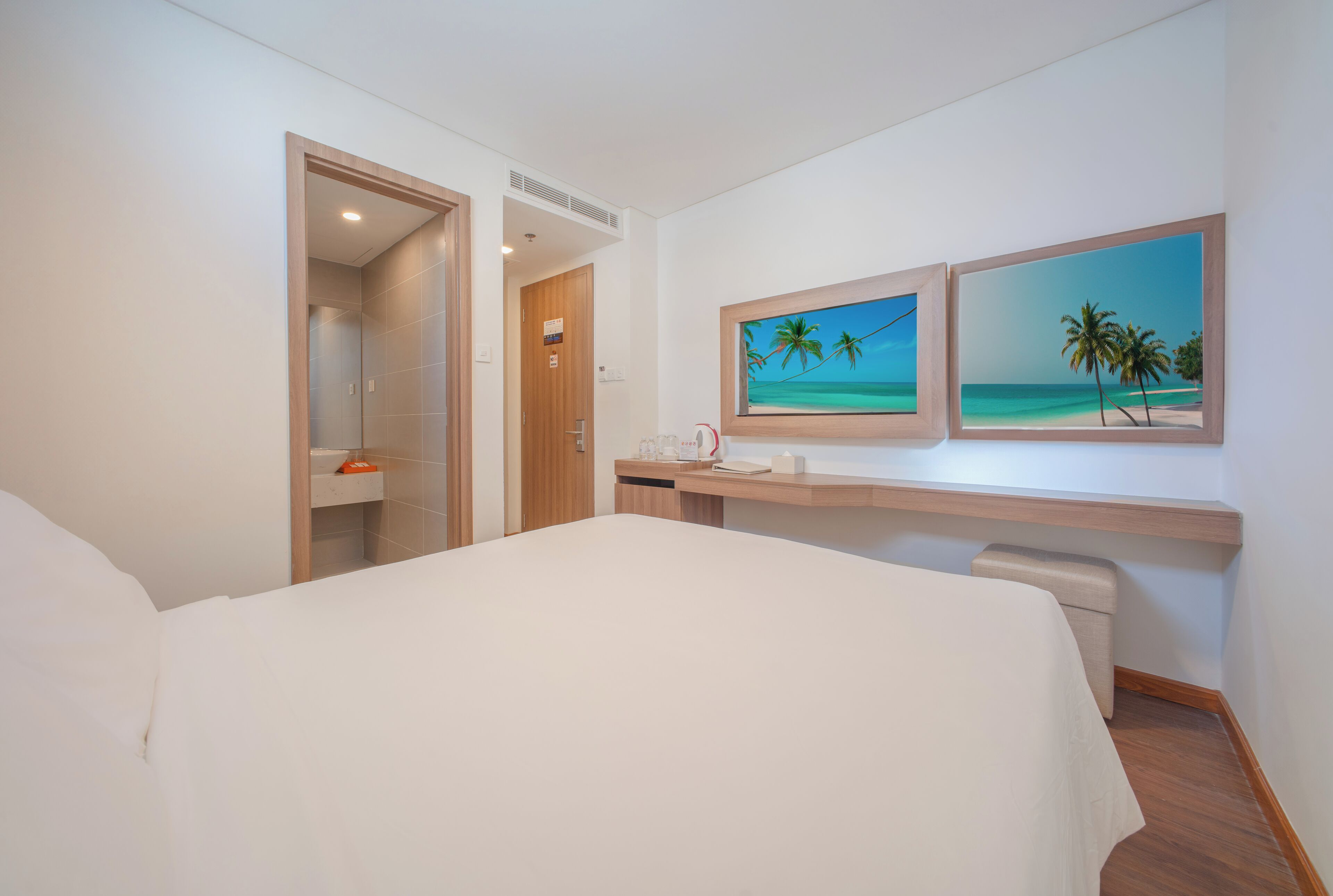 Habitación de hotel con una cama, un escritorio y dos cuadros enmarcados con una playa.