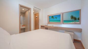 Habitación de hotel con una cama, un escritorio y dos cuadros enmarcados con una playa.