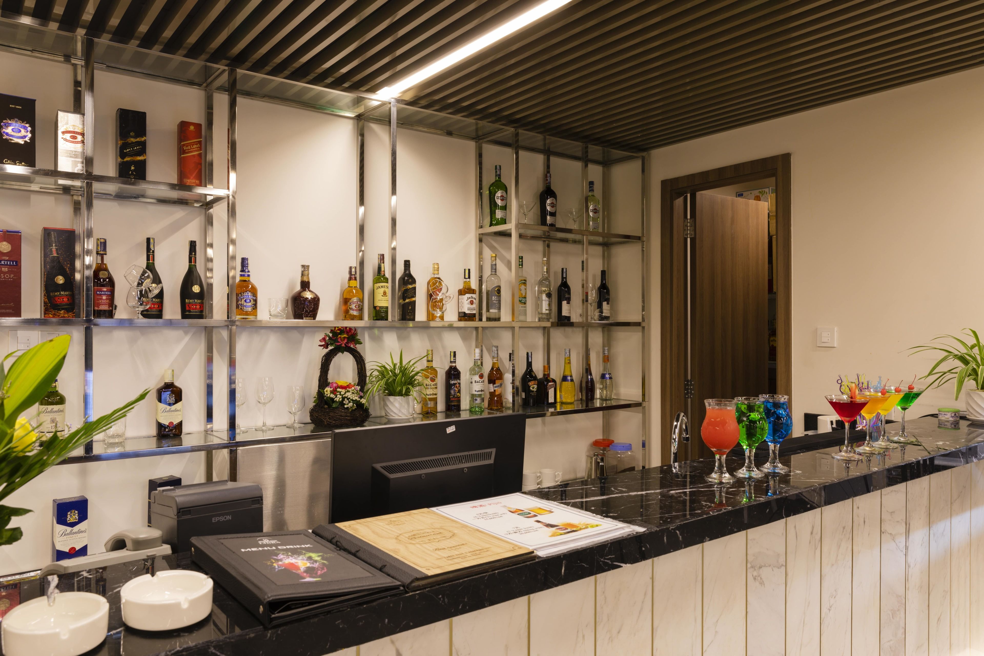 A bar area with shelves of liquor bottles, a countertop with a menu, and a potted plant.