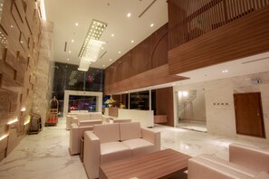 Eine moderne Lobby mit Marmorböden, komfortablen Sitzmöglichkeiten, einem Empfangstresen und einer hohen Decke mit eingelassener Beleuchtung.