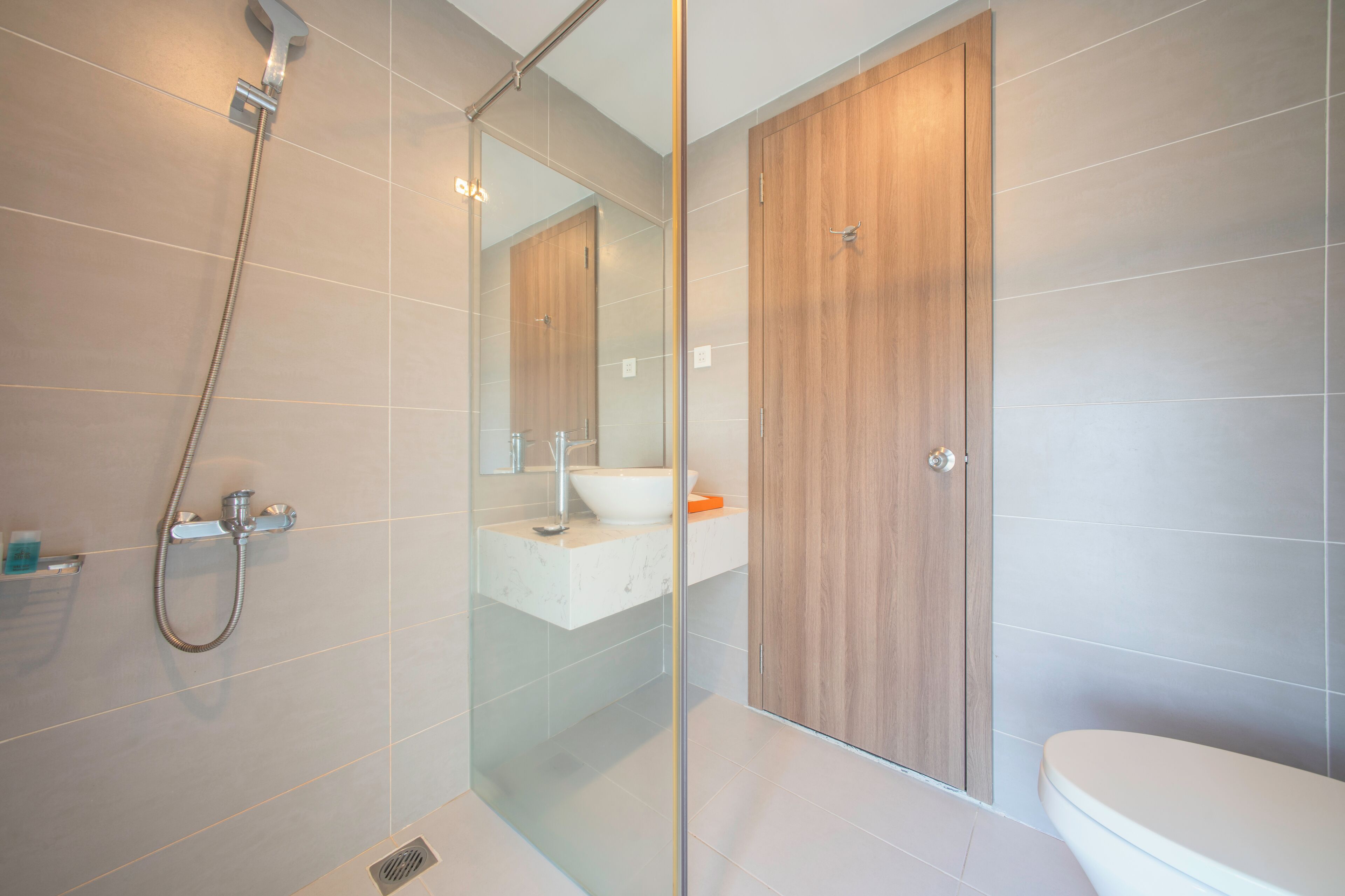 A modern bathroom with a glass shower enclosure, a wooden door, and a white sink.