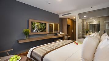 A modern hotel room with a large bed, a desk, a mirror, and a bathroom with a glass shower.