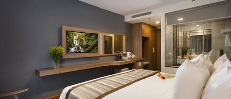 A modern hotel room with a large bed, a desk, a mirror, and a bathroom with a glass shower.