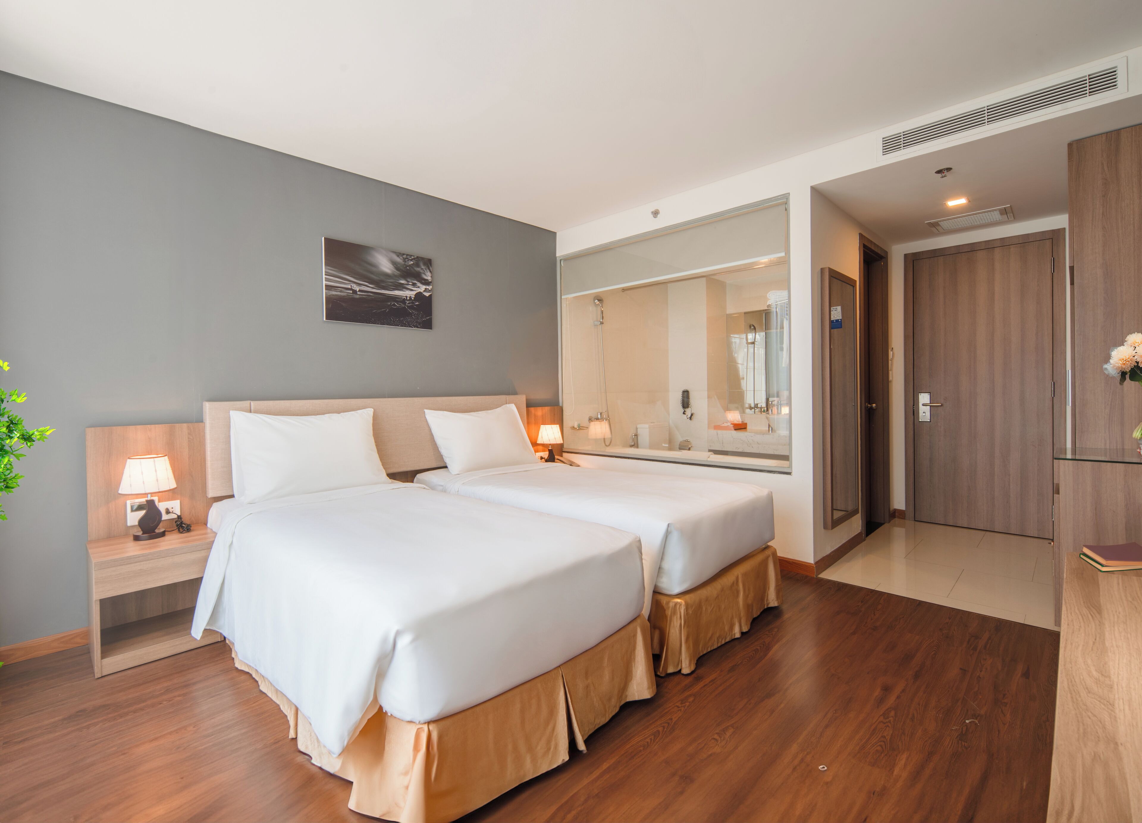 A hotel room with two beds, a nightstand with a lamp, a mirror, and a wooden wardrobe.
