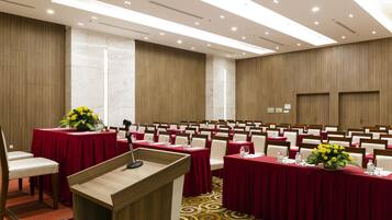 A conference room with rows of tables, each with a red tablecloth and a microphone stand.