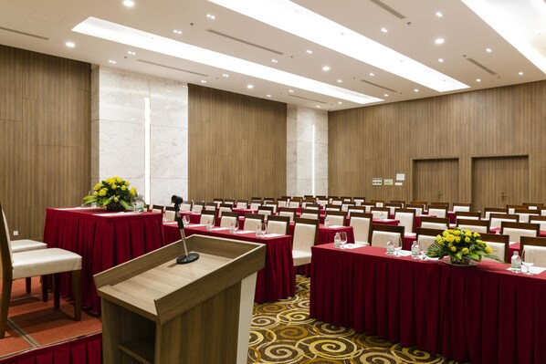 A conference room with rows of tables, each with a red tablecloth and a microphone stand.