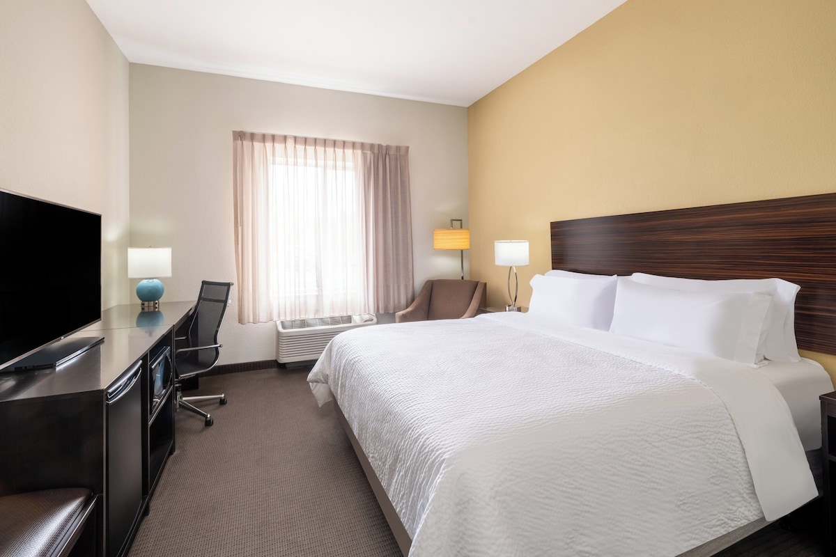 Habitación de hotel con una cama grande, un escritorio con televisor, una silla y una lámpara.
