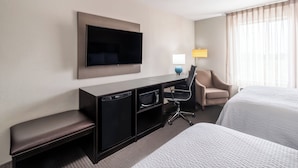 A hotel room with a flat-screen TV mounted on the wall, a desk with a lamp, a chair, and two beds. - Garner Hotel Clarksville Northeast by IHG (Clarksville)