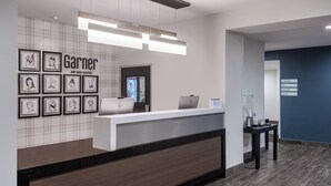 A hotel reception area with a modern design, including a reception desk, framed artwork on the wall, and a sign indicating the hotel name. - Garner Hotel Clarksville Northeast by IHG (Clarksville)