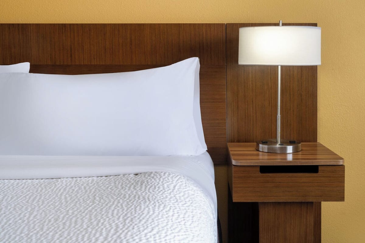 A neatly made bed with white linens and a wooden headboard.