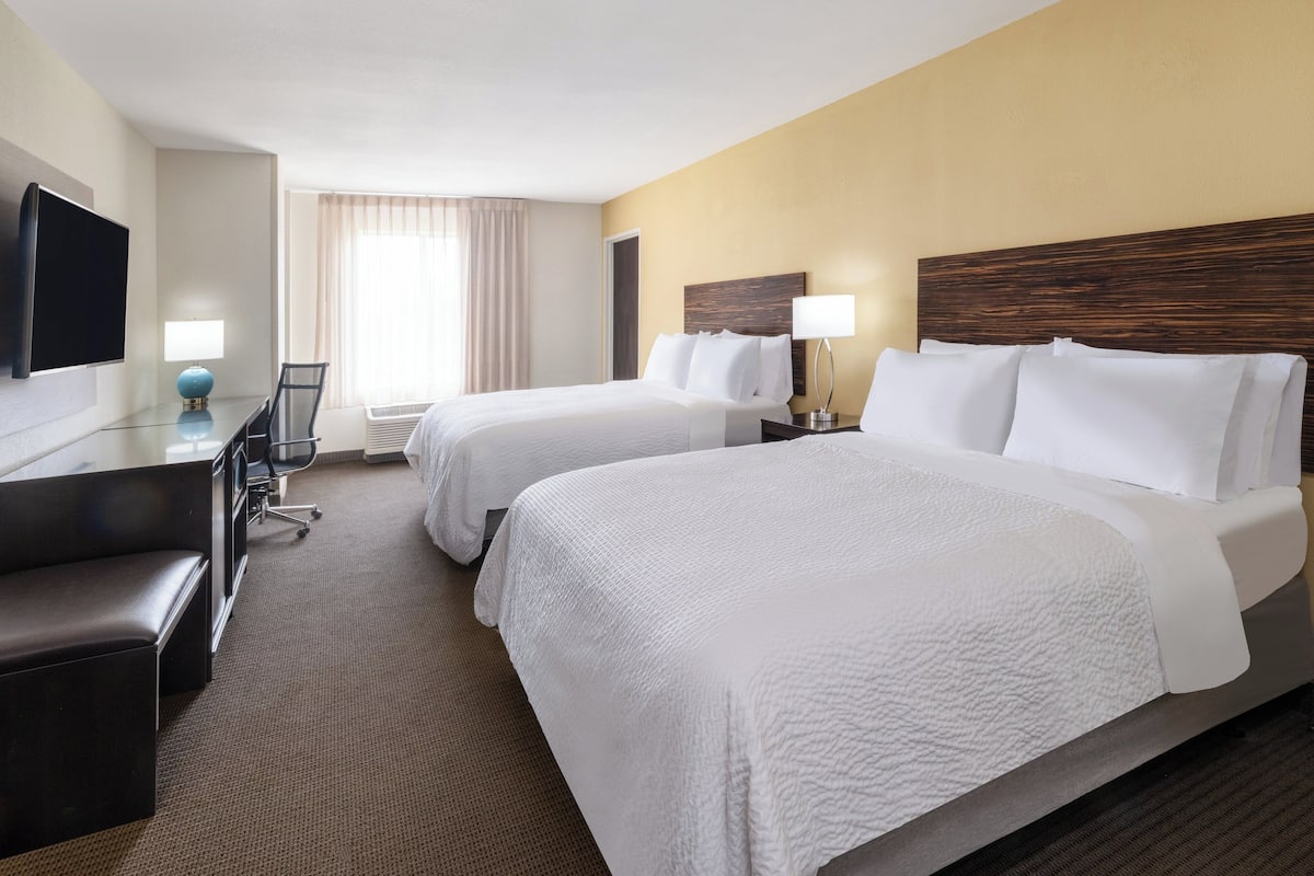 A hotel room with two beds, a desk, a chair, a TV, and a window with curtains.