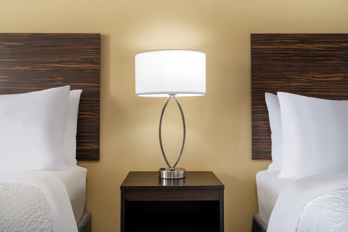 A hotel room with two beds, a nightstand with a lamp, and a wooden headboard.