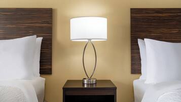 A hotel room with two beds, a nightstand with a lamp, and wooden headboards.