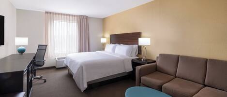 Una habitación de hotel con cama, escritorio, silla, sofá y televisión.