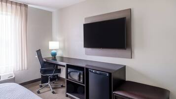 Habitación de hotel con una cama, un escritorio con ordenador, microondas, frigorífico, televisión y ventana con cortinas.