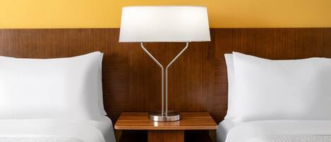 Una habitación de hotel con dos camas, una mesita de noche de madera y una lámpara de mesa moderna.