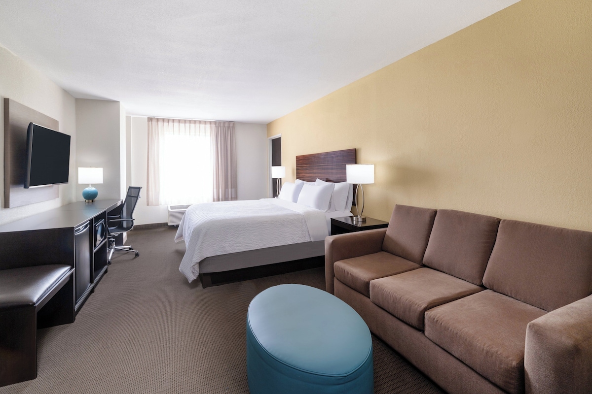 Una habitación de hotel con cama, sofá, escritorio, televisor y lámpara.