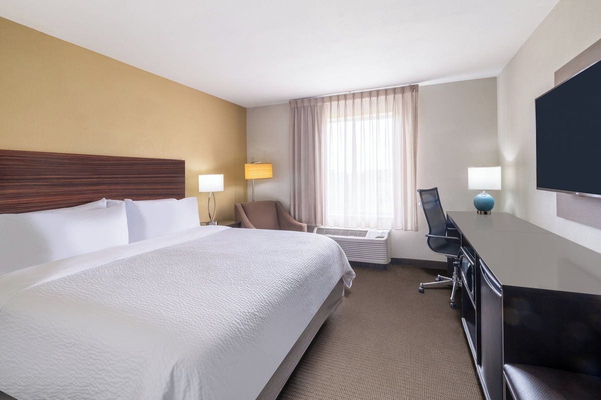 Habitación de hotel con una cama grande, un escritorio con silla, un televisor de pantalla plana, un equipo de aire acondicionado y una ventana con cortinas.