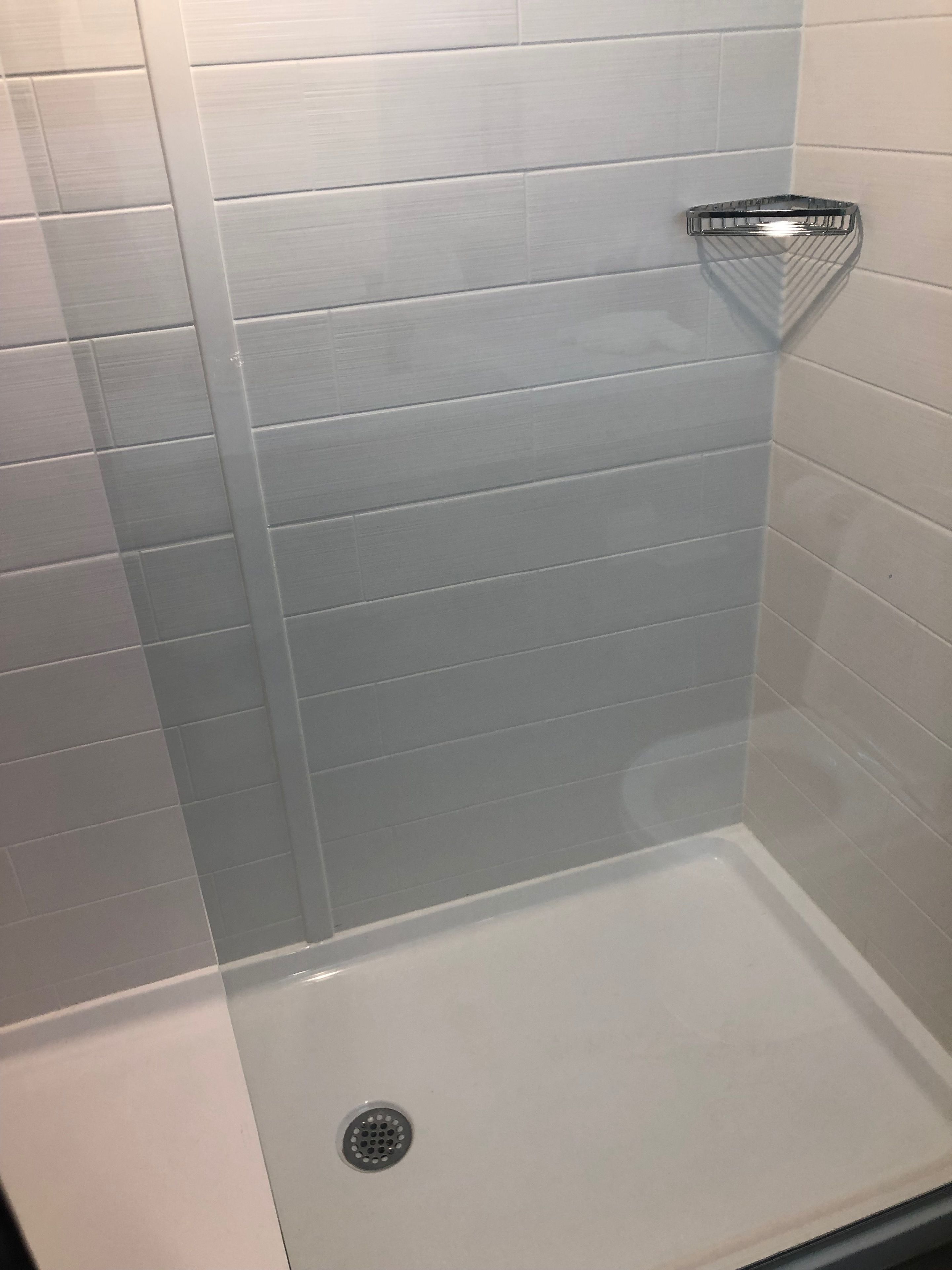 A shower with a glass door, white tiled walls, and a chrome shower head.