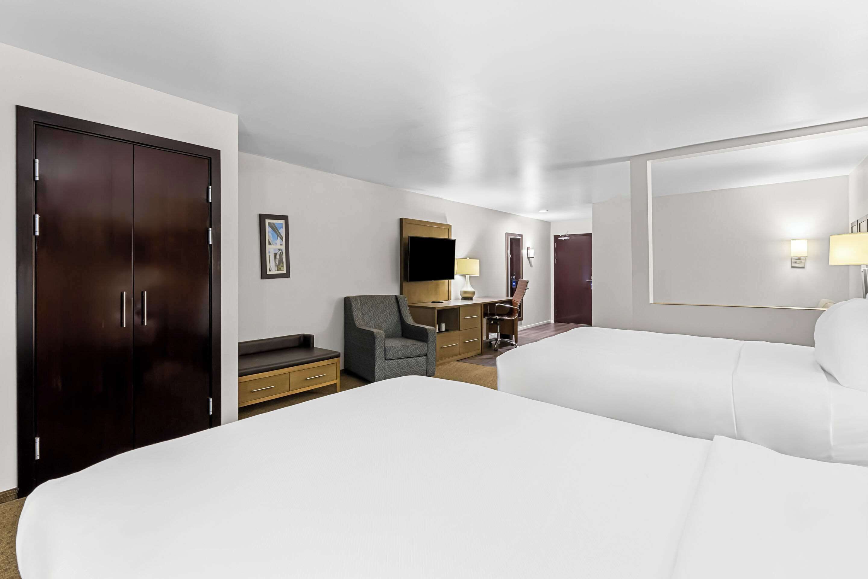 Une chambre d’hôtel avec deux lits, un bureau avec une chaise, une armoire et un téléviseur.
