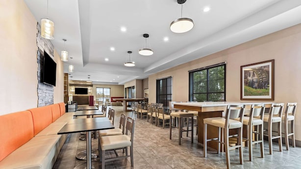 A spacious dining area with high tables and chairs, a long orange bench, and a TV mounted on the wall. - Comfort Suites Columbia I-65 (Columbia)