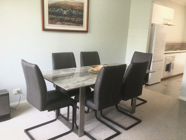 A dining area with a marble table and black chairs, a small bowl on the table, and a kitchen with a refrigerator and oven in the background.