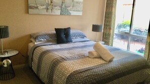 A neatly made bed with a patterned bedspread, two bedside lamps, and a painting on the wall. - Castlereagh 7 Middleton Beach Albany (Middleton Beach)