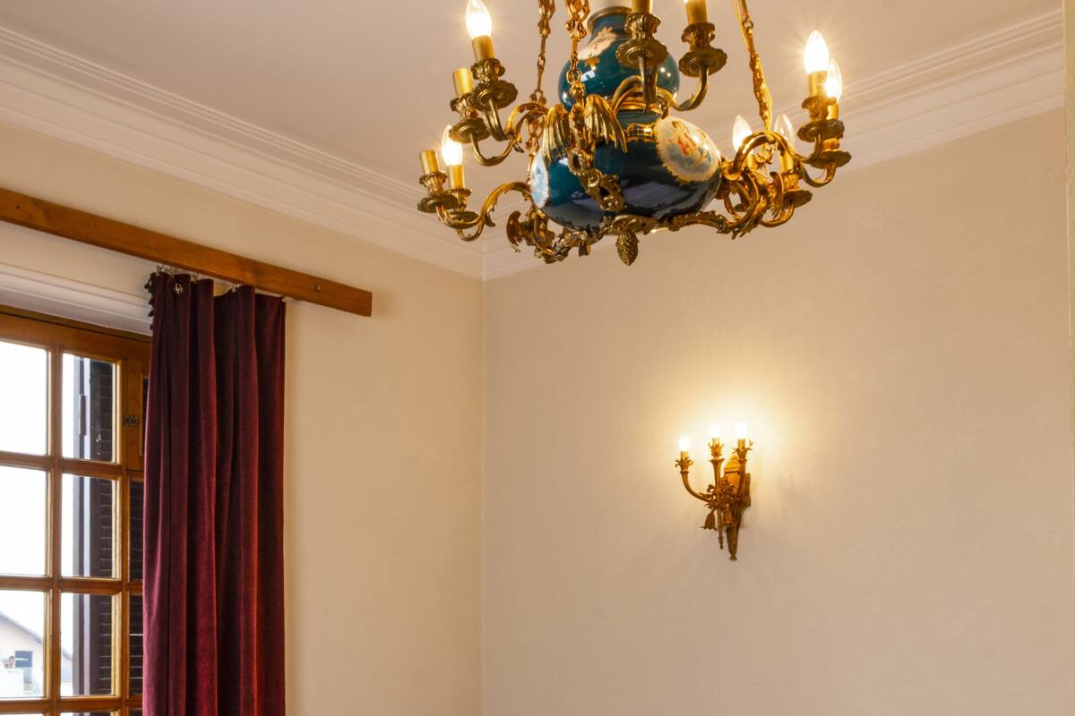 Ein Hotelzimmer mit einem großen Bett, einer Deckenleuchte, einem Fenster mit Vorhängen und einer Wandlampe.