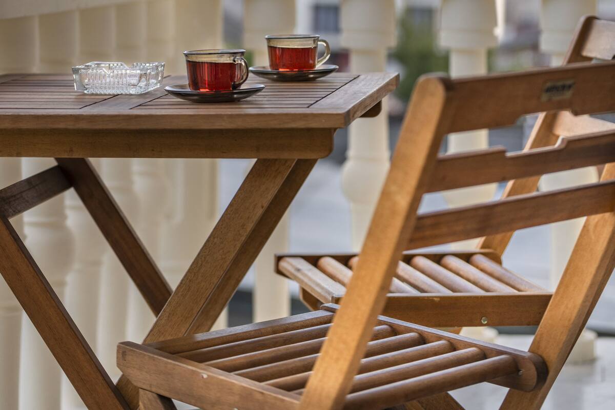 Ein Holztisch mit zwei Tassen und einem Glas auf einem Balkon mit Blick auf Gebäude.