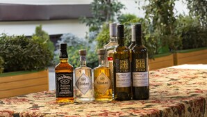 Un tavolo con bottiglie di Jack Daniel's, Midori e whisky Iveria in una zona esterna riparata, con vista su un edificio con finestra e persiane.