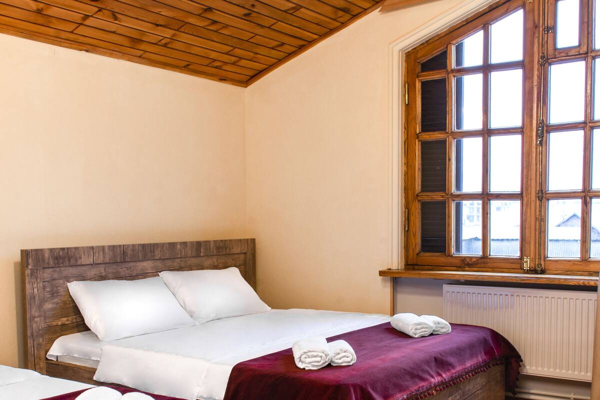 Ein Zimmer mit zwei Holzbetten, einem großen Fenster und einer Holzbeschichtung an der Decke.