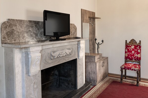 Una chimenea con un televisor encima, un espejo arriba y un sillón tapizado rojo a la derecha.