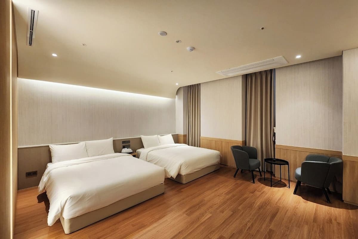 A hotel room with two beds, a seating area with chairs, and a wooden floor.