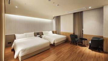 Habitación de hotel con dos camas, zona de estar con sillas y piso de madera.