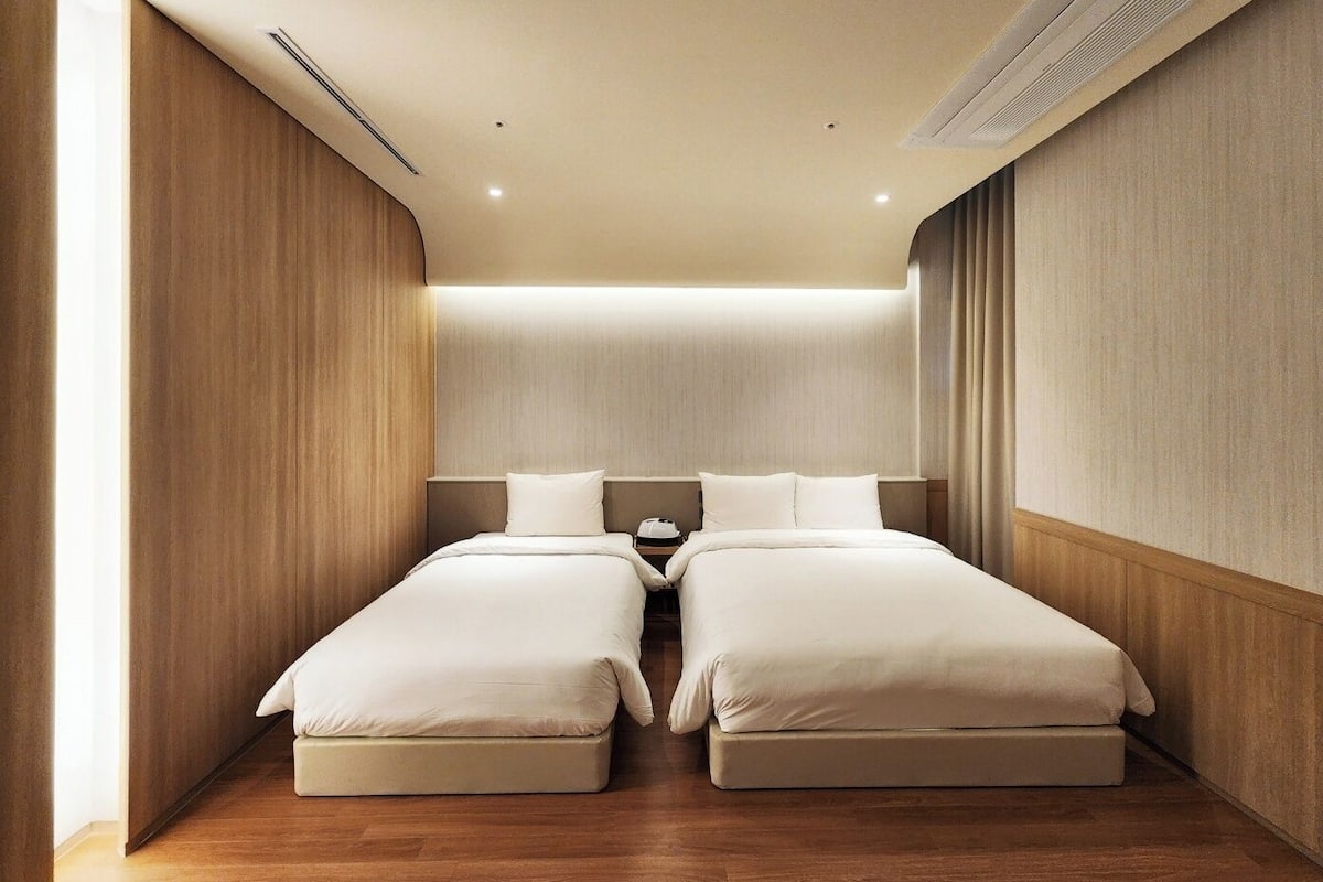 A modern hotel room with two beds, wooden paneling, and a wooden floor.